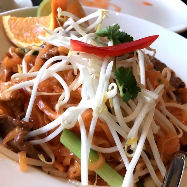 Close-up of My Thai Pad See Ew noodles with bean sprouts, red pepper, and orange slice.