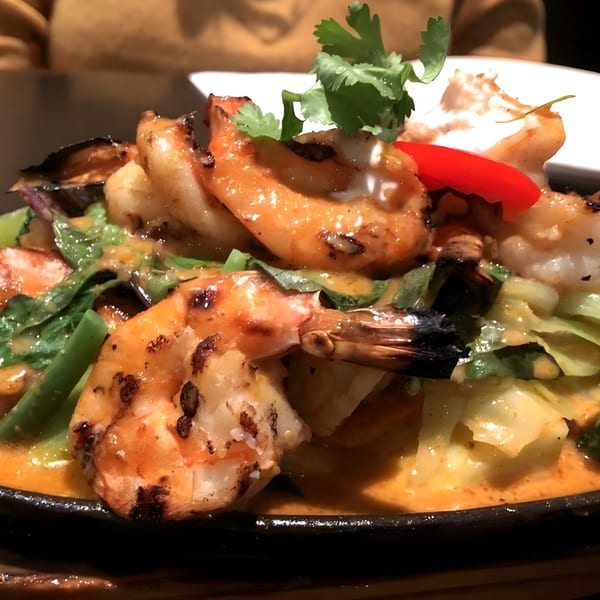 Grilled shrimp with red curry sauce, green vegetables, and cilantro in a black bowl.