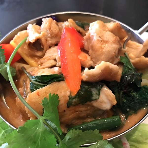 Close-up of My Thai red curry with chicken, bell peppers, and green vegetables in a silver bowl.